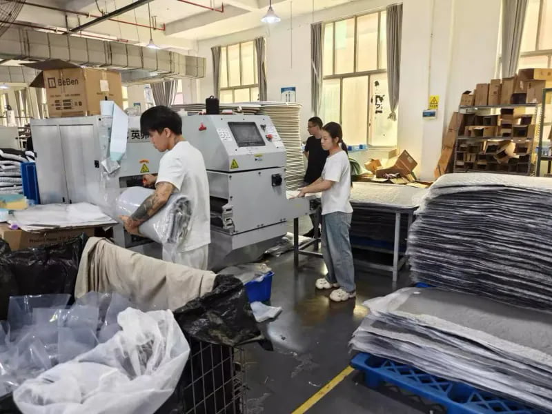 Workers packing pet bed products beside bagging equipment