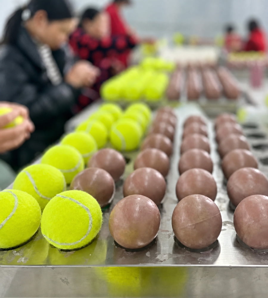 Natural rubber ball cores beside felt-covered dog tennis balls during production