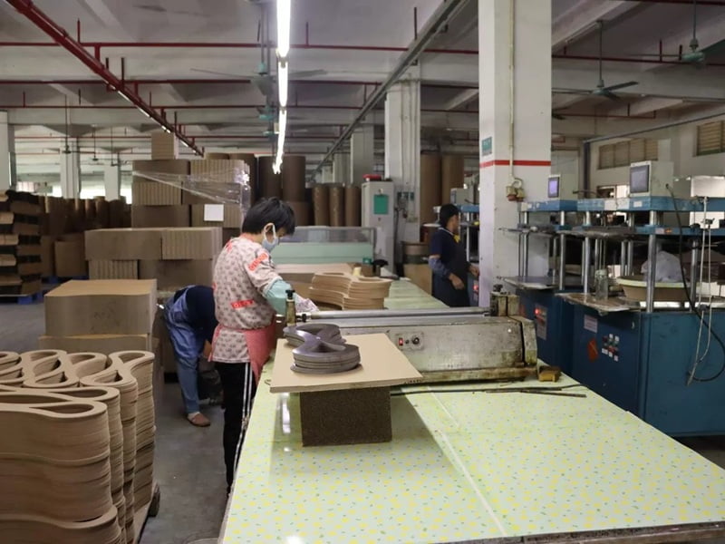 Workers operating bonding and pressing equipment during corrugated cat scratcher production
