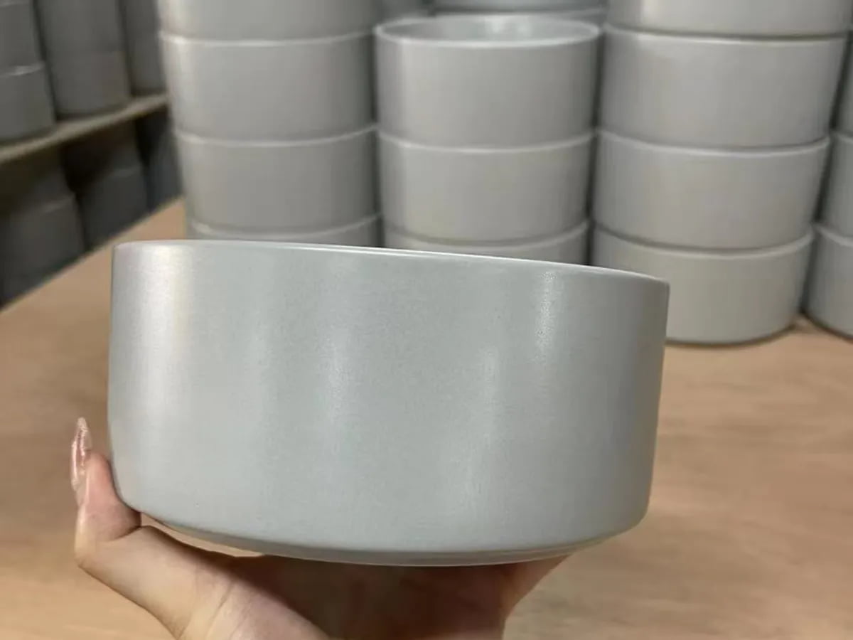 Hand holding a gray ceramic pet bowl with matching bowls stacked in the background