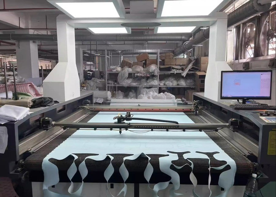 Cutting machine with dog-harness-shaped fabric panels on the cutting bed.