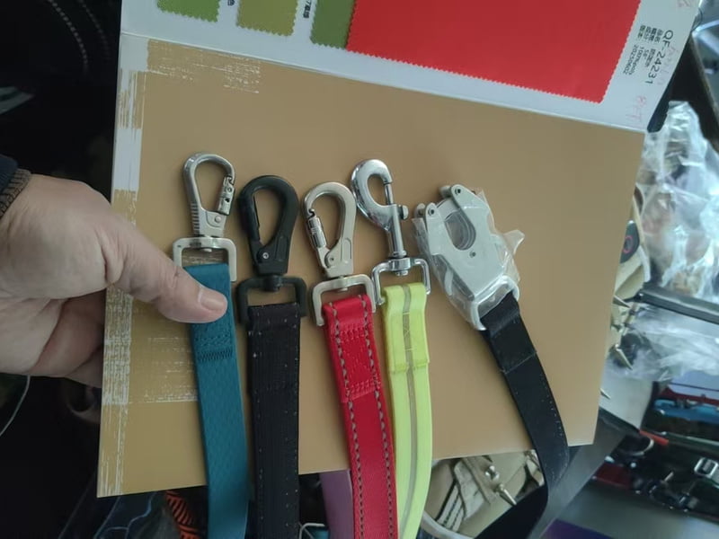 Five dog leash hooks attached to webbing straps, showing different clip designs and finishes.