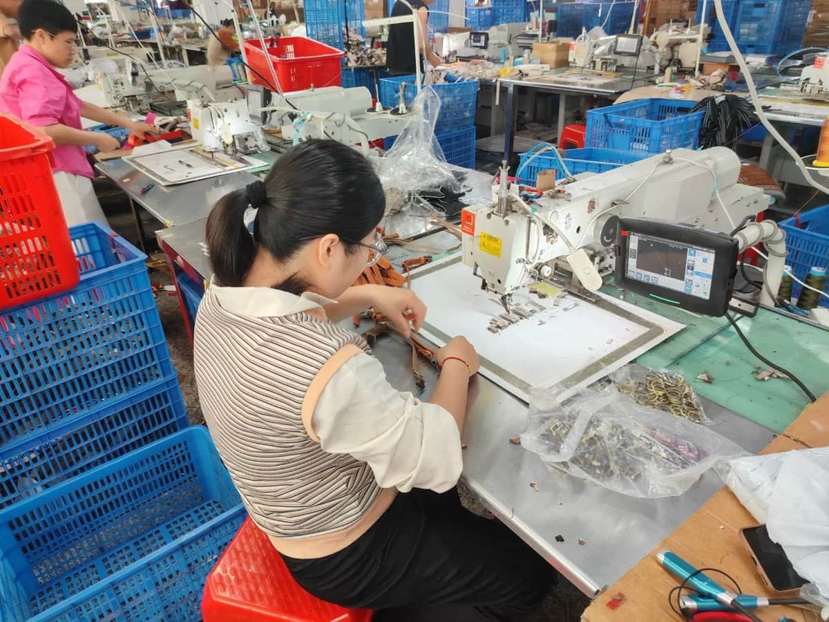 Worker preparing straps at a sewing station with metal rings and other components on the table