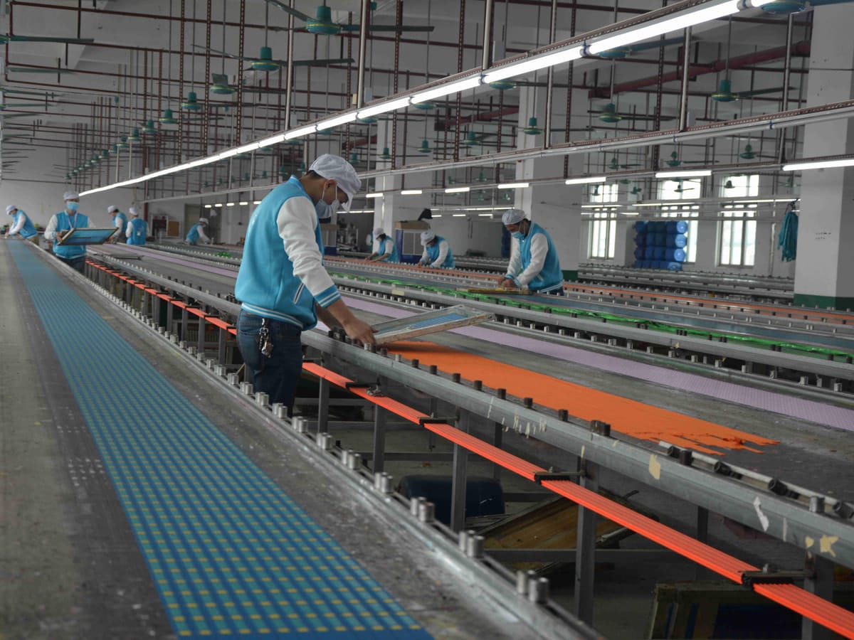 Workers screen printing colored webbing on long production tables