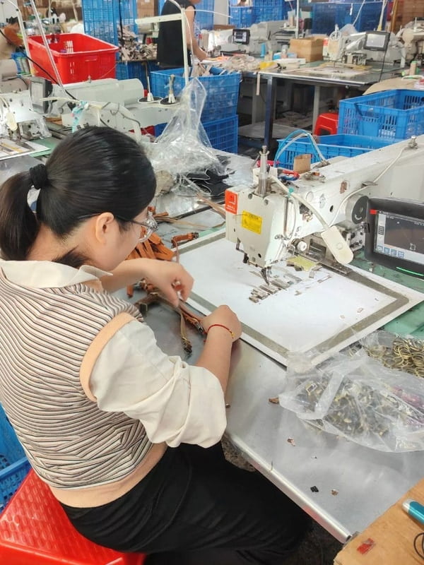 Worker preparing straps and metal rings beside a computerized sewing machine