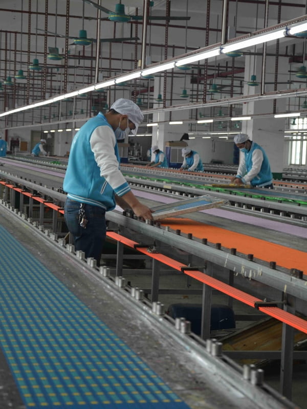 Workers screen printing patterns onto pet collar webbing on long printing tables