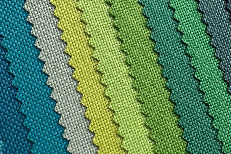 Overlapping woven fabric swatches in blue, gray, yellow and green shades, showing texture and zigzag-cut edges.
