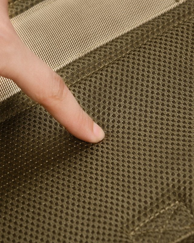 Finger pressing khaki mesh lining inside a pet harness, showing the mesh texture and stitched panels.