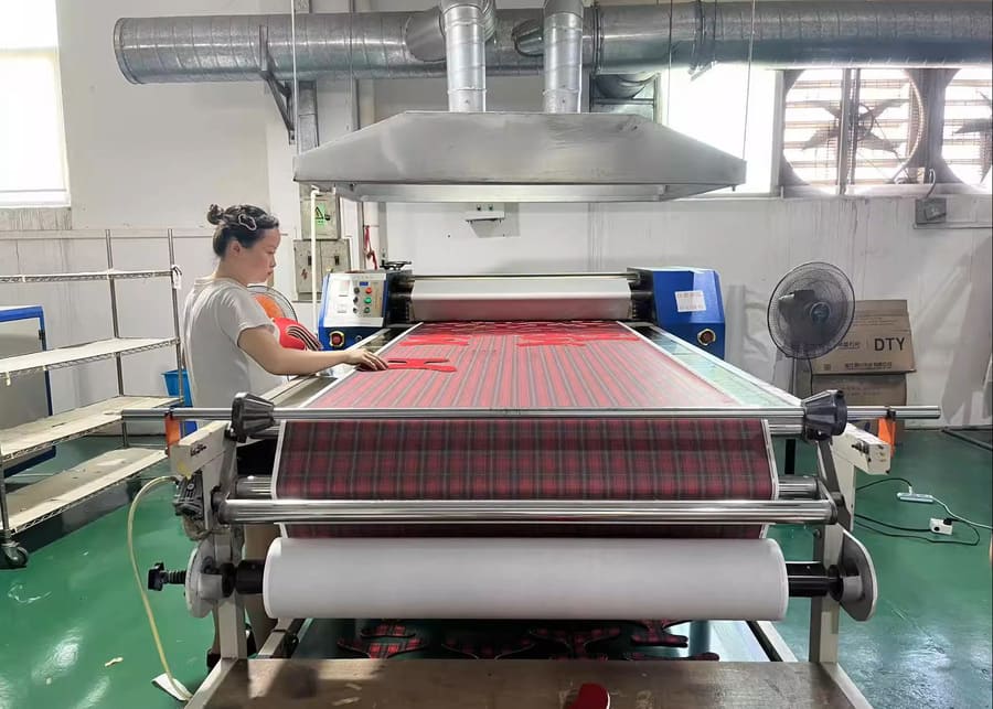 Worker feeding patterned fabric through a roller machine in the factory.