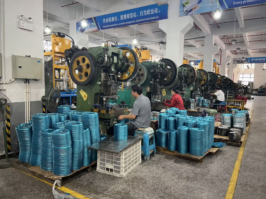 Workers operating presses beside stacks of stainless steel pet bowl parts