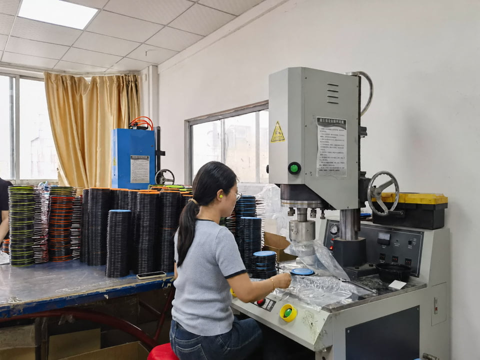 Worker at a collapsible pet bowl workstation beside stacks of folded bowls