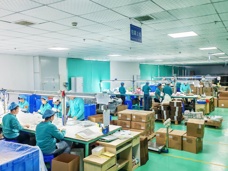 Workers packing pet bowls at worktables with packaging materials and shipping cartons